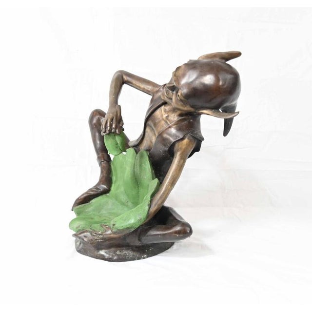 A charming bronze garden sculpture depicting a playful seated pixie or woodland fairy the animated figure wears a pointed...