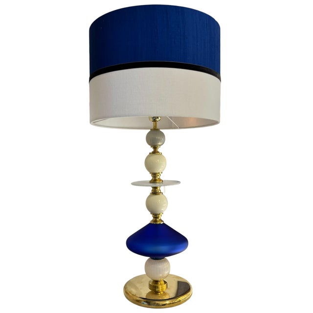 Table lamp with a central structure composed of blown glass and brass elements, with translucent white and blue details...