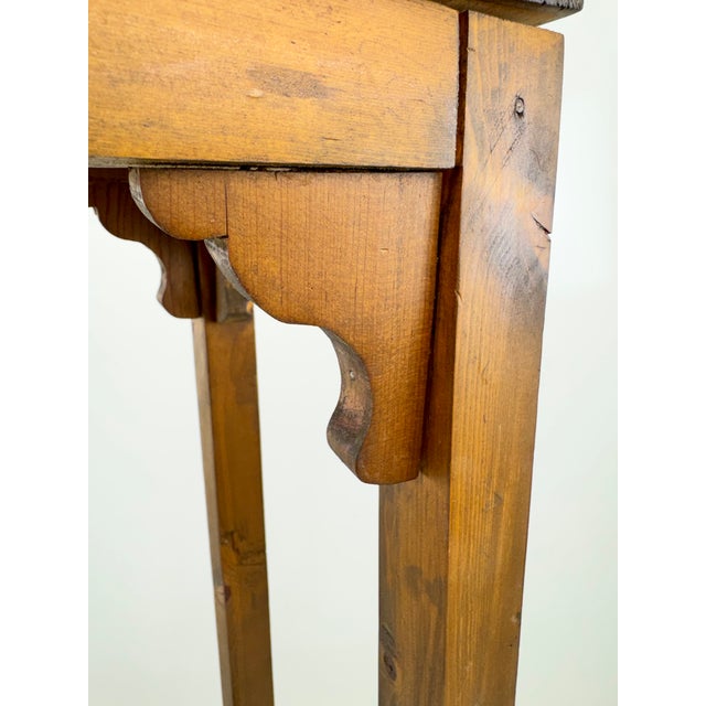 A charming vintage wooden pedestal stand featuring a warm honey-brown finish and a tall, slender silhouette. The square...