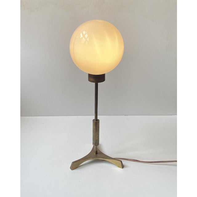 A rare table lamp composed of solid patina brass and mounted with an opaline glass sphere. Stylistically is tics all the...