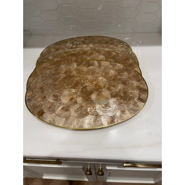 Beautiful set of 12 Capiz champagne-colored oval placemats with a brass rim around each one. They are cork-backed. Made in...