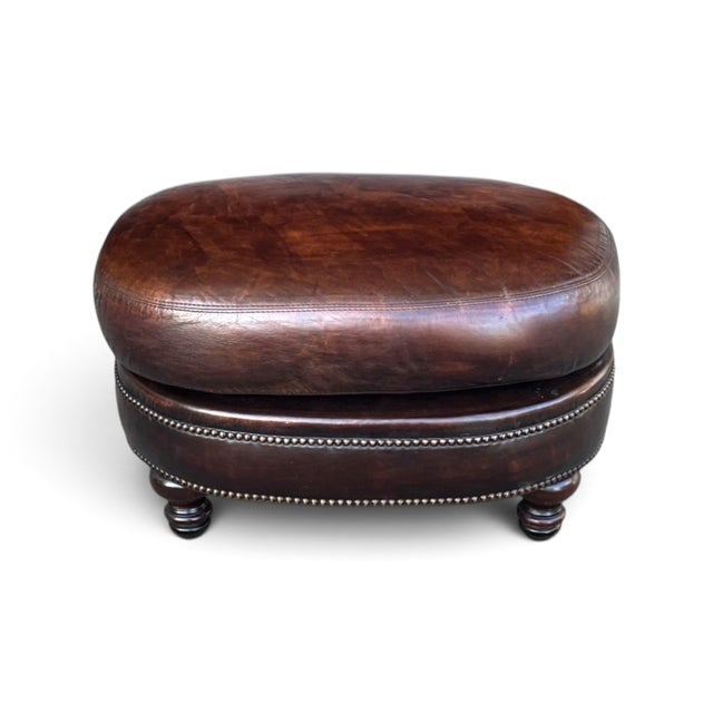 This distinctive vintage oval ottoman is upholstered in rich brown leather with a beautifully developed natural patina,...