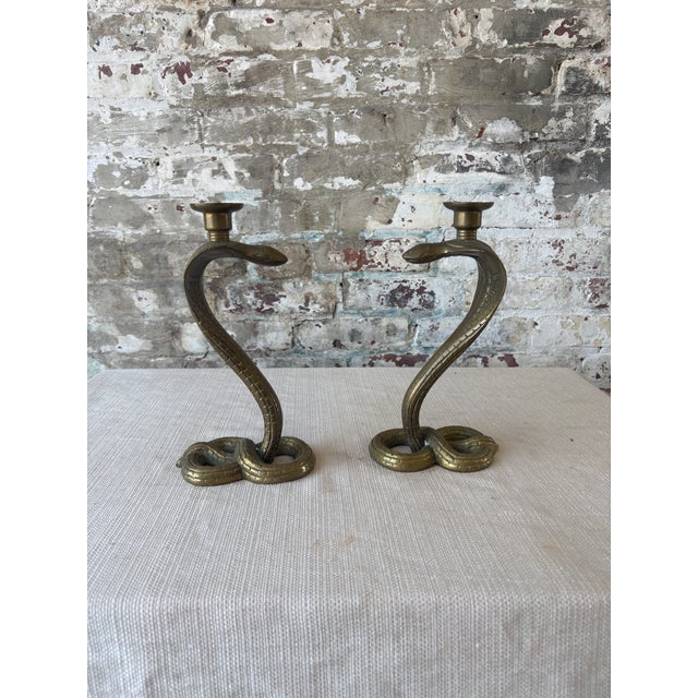 An eye-catching pair of vintage solid brass cobra candlestick holders featuring sculptural rearing snakes with coiled...