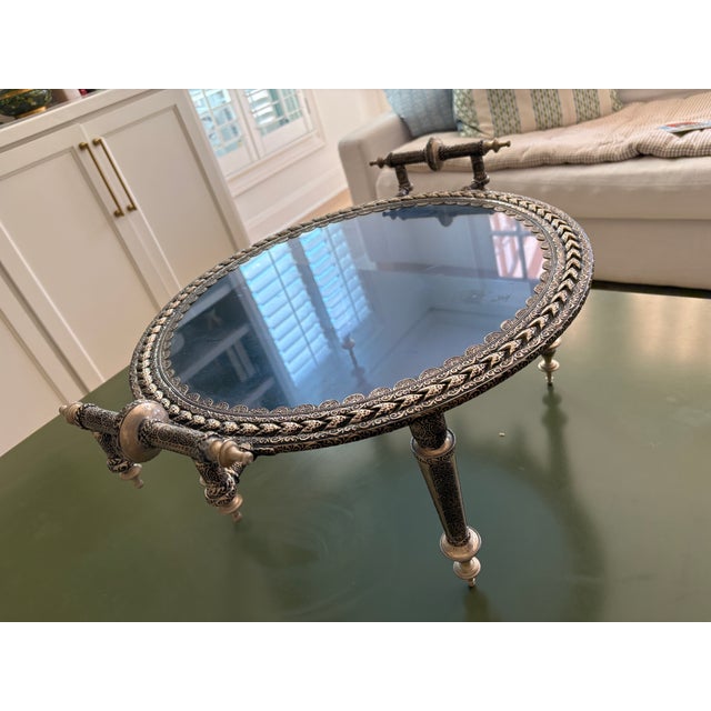 A striking Moroccan footed tray in hand-chased silver-tone metal, finished with richly detailed arabesque, scrolling vine,...