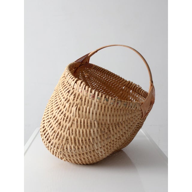 This sculptural vintage wicker buttocks basket features a rounded handwoven form, open lattice weave, and a bentwood...