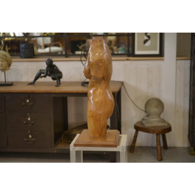 A 1960s oak sculpture of a nude figure, sculpted in the round. The stylized female body is depicted as a bust, with soft...