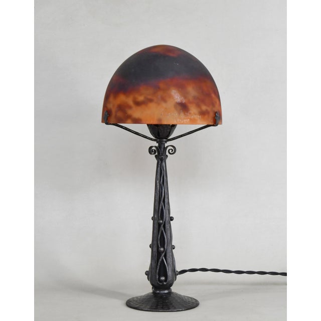 Daum A 1925-1930 French art deco lamp in wrought iron. The excellent forged base holds a beautiful Daum shade in colored...