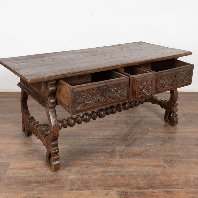 Dark walnut console table with three drawers resting on harp shaped legs and decorative turned stretcher. Elaborate hand...