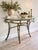 Elegant vintage glass-top console table featuring an exceptionally ornate metal base with an antiqued gilt bronze finish,...