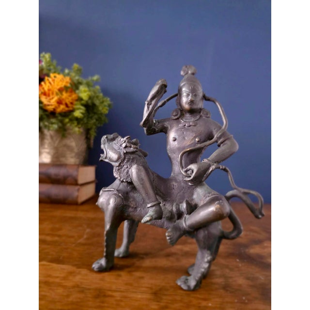 Striking antique Indian bronze sculpture depicting a dynamic deity figure seated upon a stylized lion, richly adorned with...