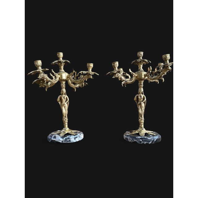 A pair of finely chased gilt bronze candelabra resting on circular bases of veined black marble. each stem is adorned with...