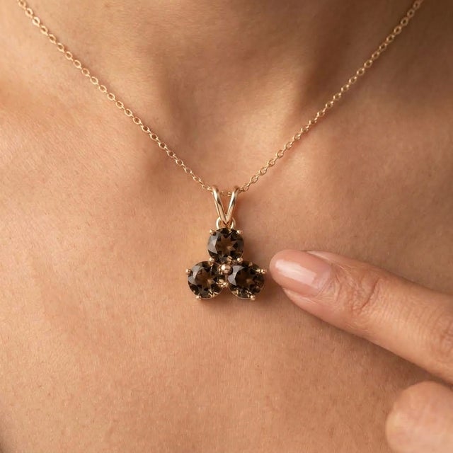 An earthy three-stone design featuring round-cut natural smoky quartz arranged in a graceful trefoil formation, secured in...