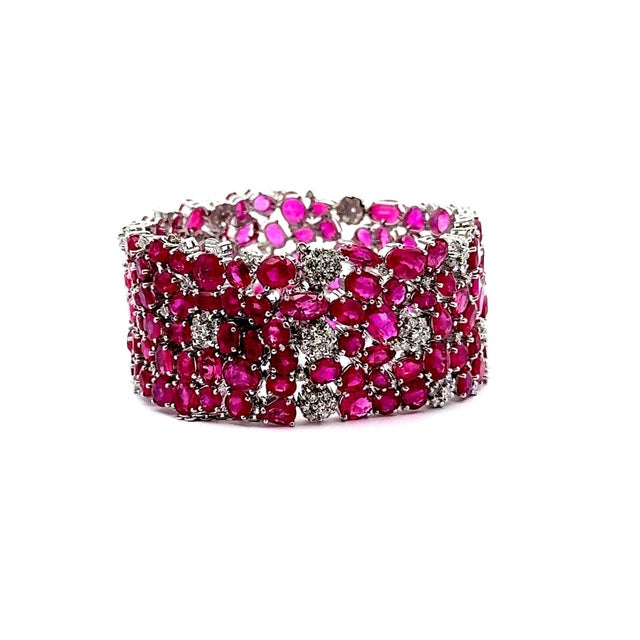 A striking bracelet showcasing a vibrant array of mixed-cut rubies and round-cut diamonds. The rubies, weighing 89.86...