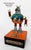 This mixed media assemblage features a whimsical figure combining mechanical elements with playful charm, depicting a dog...