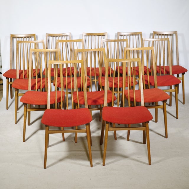 Fourteen walnut dining chairs from the 1960s with slender, tapered legs and vertical spindles in the backrest. The red...