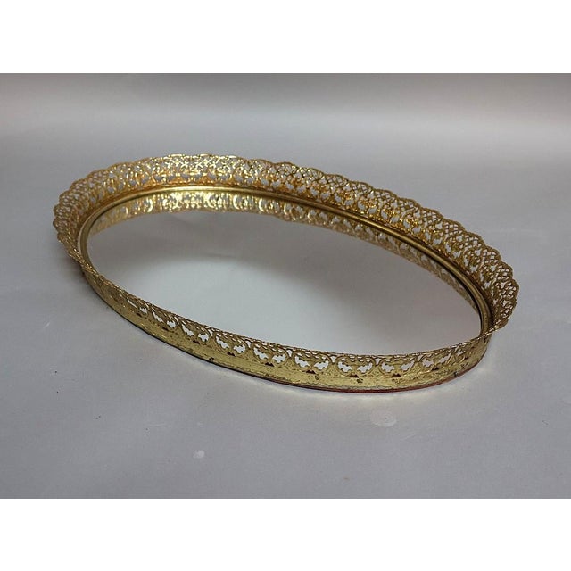 Vintage Hollywood Regency oval vanity tray featuring a mirrored glass surface surrounded by an ornate pierced brass...
