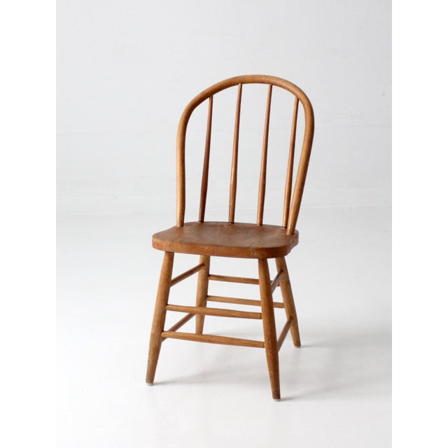 This antique Windsor style dining chair features a classic bow back silhouette with tall spindle supports, a shaped wood...