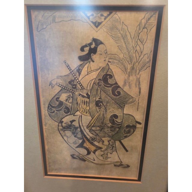 Framed Japanese figurative print depicting a traditionally dressed figure carrying swords, rendered in a dramatic ukiyo-e...