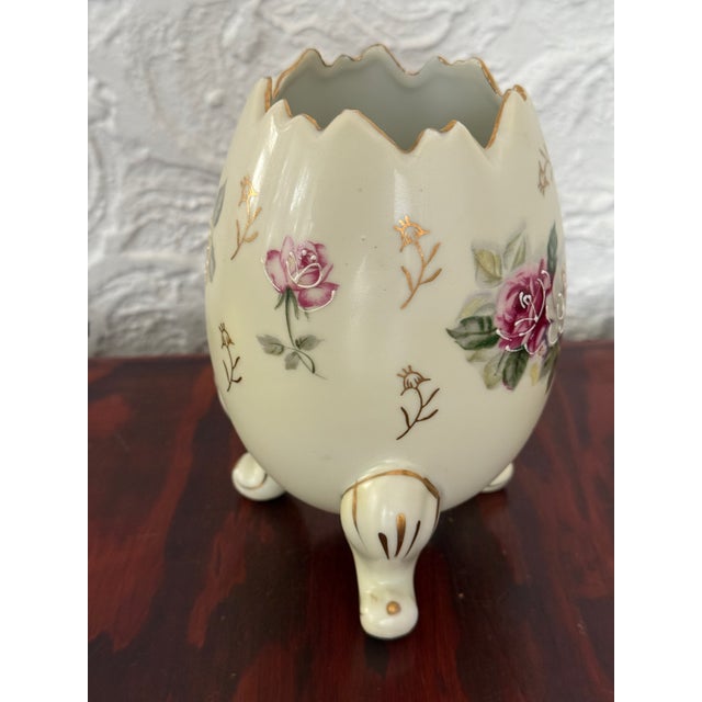A midcentury porcelain egg-shaped vase from Japan. Stands on three scrolled feet. The cream body is hand painted with...