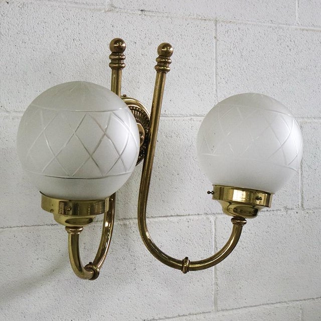Golden brass wall light produced in the 1950s with two arms and two glass lampshades. Compatible with E27 type bulbs....