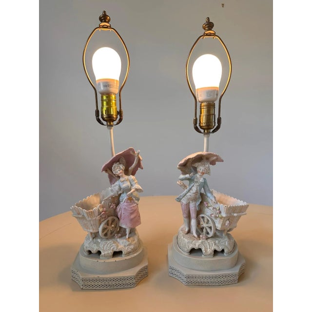 Antique German bisque figural base lamps, male and female figures with flower carts, pastel glazes.