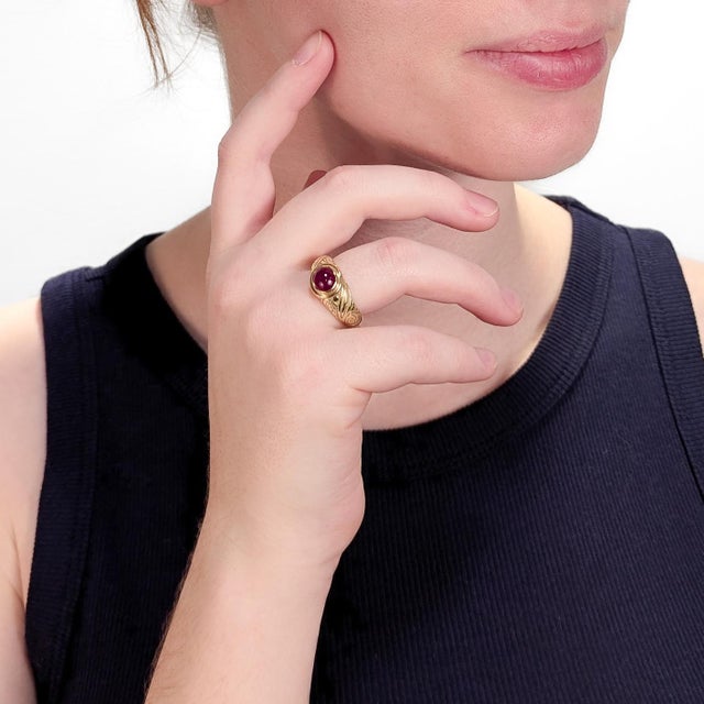 A fine gold & ruby ring. In 18 karat yellow gold. With a bezel-set opaque ruby cabochon, engraved decoration to the...