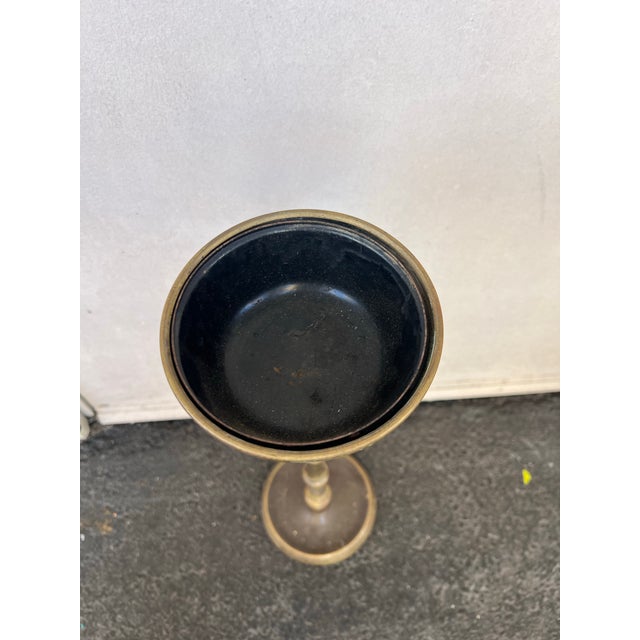 This vintage brass standing ashtray features a tapered column stem and a round base, displaying a natural green patina...