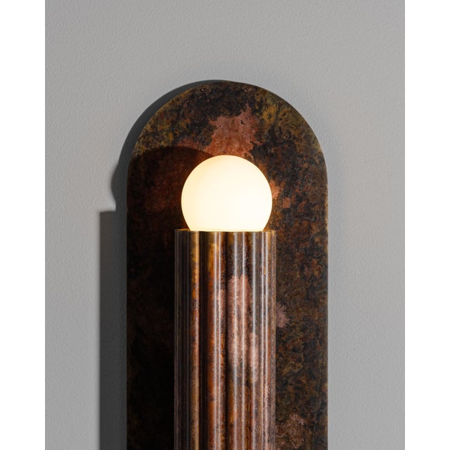 A single fluted cylinder rests on an oval plate, its geometry distilled to pure form. Entirely crafted in solid brass, it...