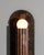 A single fluted cylinder rests on an oval plate, its geometry distilled to pure form. Entirely crafted in solid brass, it...