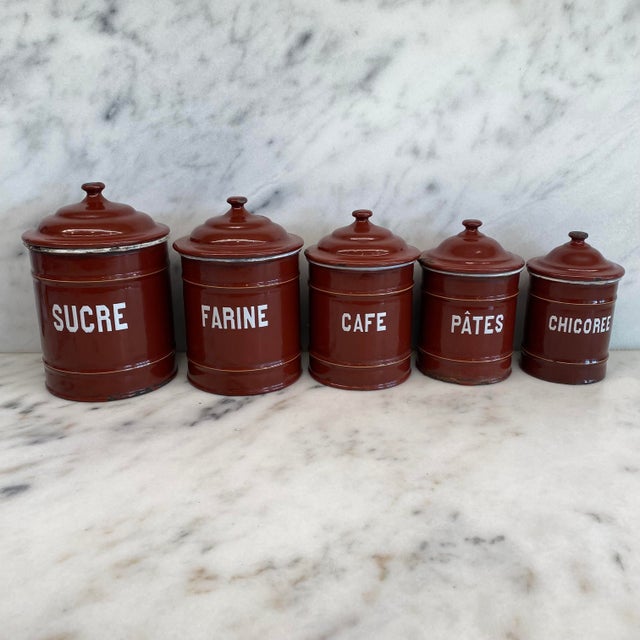 A charming set of five French enamel kitchen canisters in a rich reddish brown finish with crisp white lettering and...