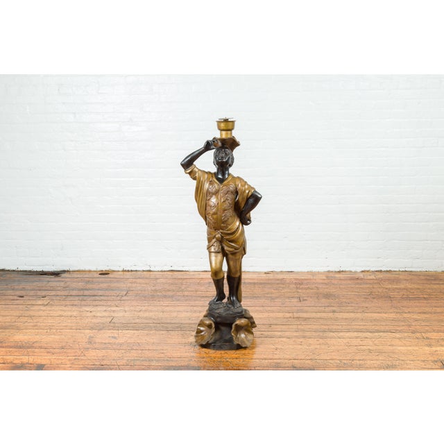 A vintage bronze candleholder statue with black and gold patina, on shell base. Created during the 20th century with the...