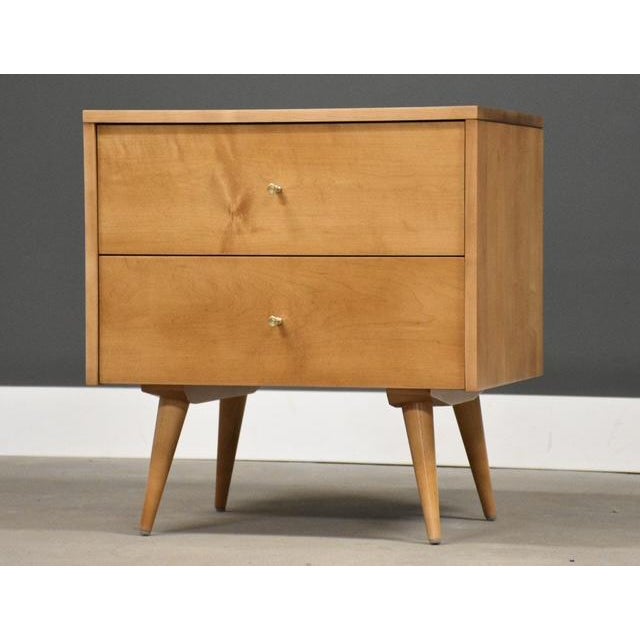 A mid century modern solid maple two drawer nightstand with polished brass hourglass knobs and canted legs designed by...