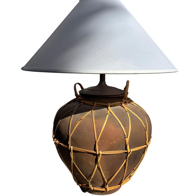 Stoneware water jar table lamp with woven rattan detailing. Unglazed clay vessel with original rattan wrapping and loop...