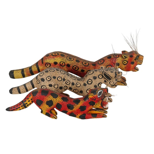 A set of three carved big cats. A tiger, a snow leopard, and a serval are carved in wood and vibrantly decorated in...