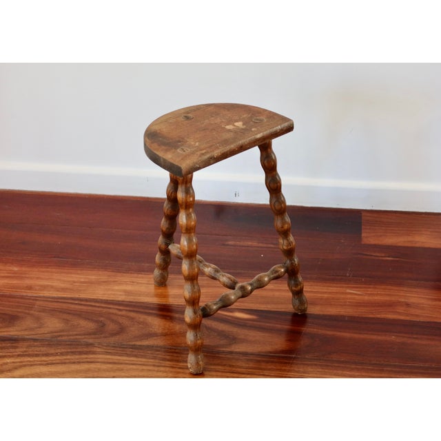 Antique tripod stool in turned wood, characterized by its twisted legs connected by a carved stretcher that emphasizes its...
