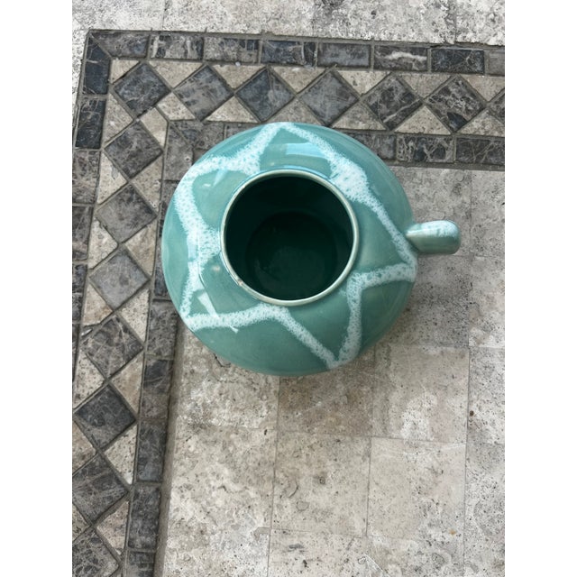 This beatiful seagrass colored glazed ceramic vase has a sunburst design and a handle like a teapot.