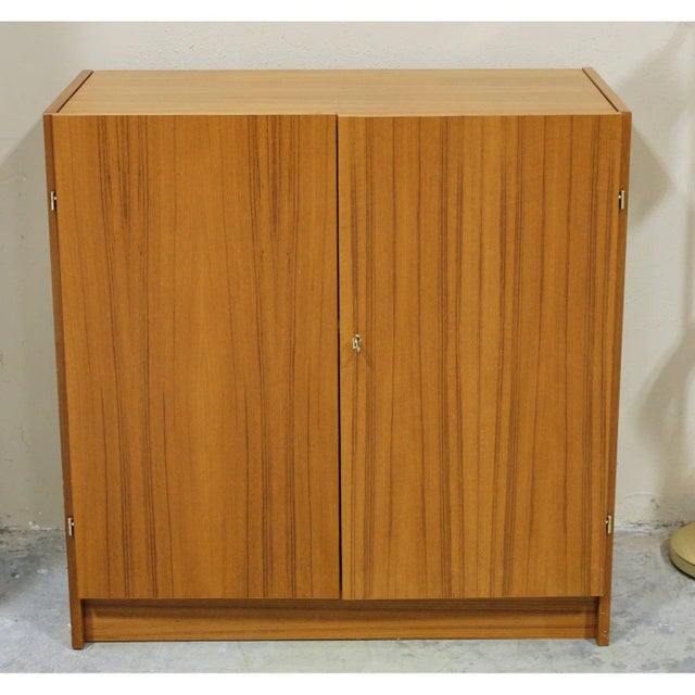 Mid-century modern teak case form with a fold-down work surface that conceals a compact workspace behind double doors. The...
