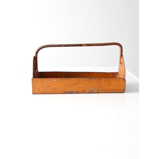 This vintage orange metal trug features a rustic design and is easily totable, making it a practical and stylish addition...