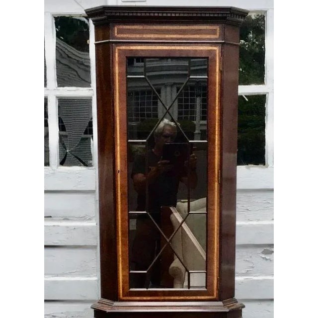 A vintage mahogany English corner display cabinet with divided glass, oval satinwood inlay and banding, and bracket feet....