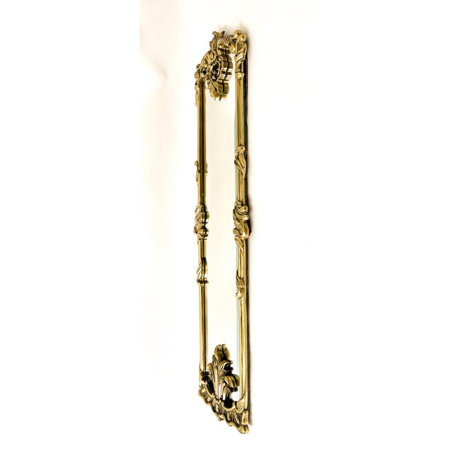 Striking vintage wall mirror framed in heavy cast brass with ornate Rococo Revival detailing. The elongated rectangular...
