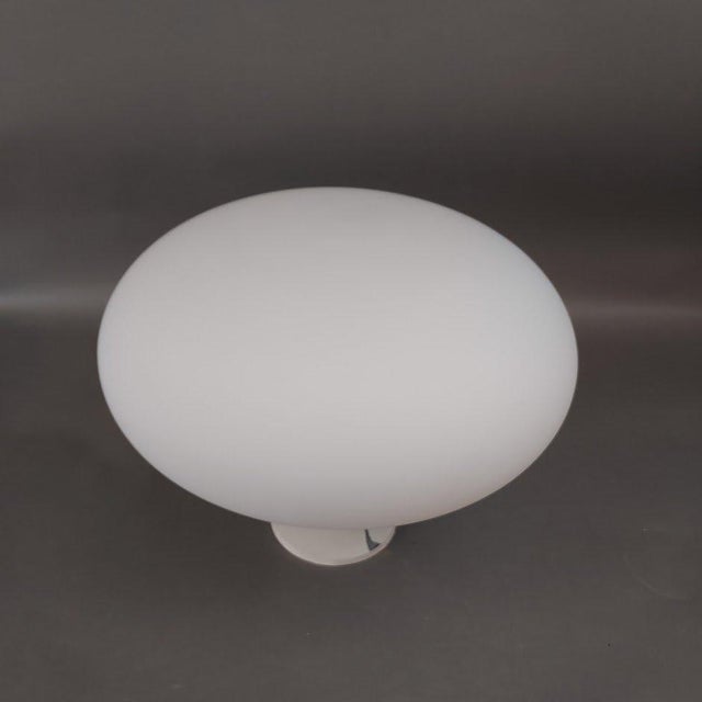 This Lightcraft ceiling light fixture features a round, white, opaque glass shade mounted to the ceiling with a white...
