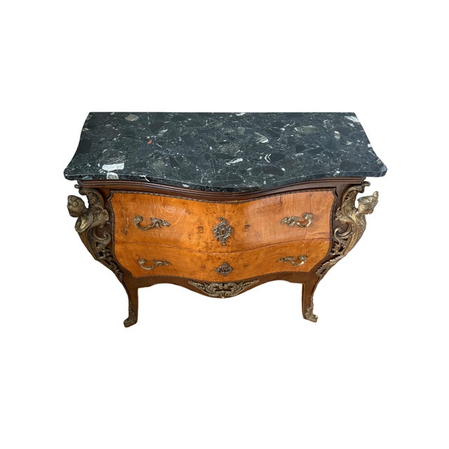 An elegant Louis XV style bombe chest featuring a dramatic serpentine profile, richly figured wood veneer, and sculptural...