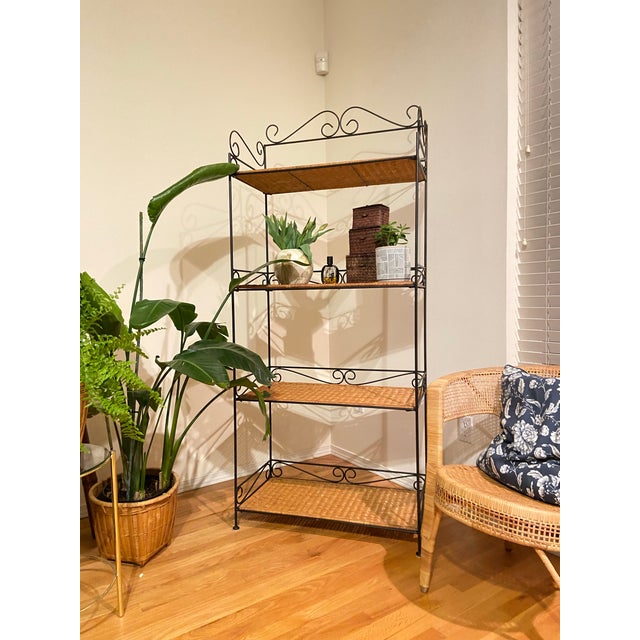 a decorative, multi-tiered wrought iron and wicker shelving unit. • Frame: Black wrought iron with intricate scrollwork...