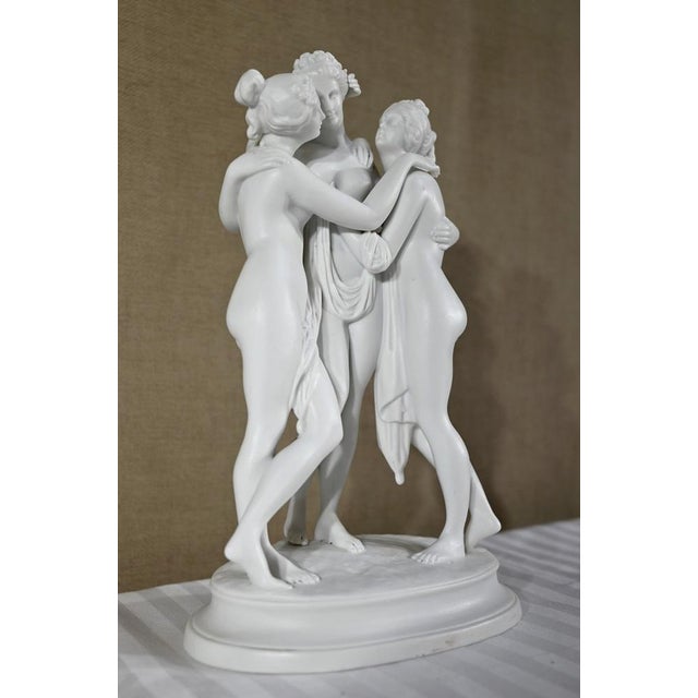 Ceramic group representing three nude nymphs with drapery, wearing flowered buns, caressing and intertwining with each...