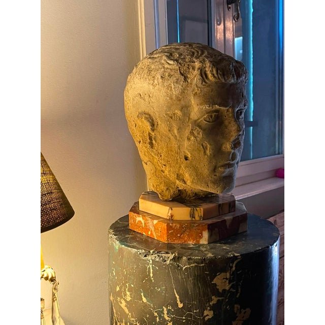 A weathered carved stone head depicting a classical youth in the Roman portrait tradition, likely a 19th-century Grand...