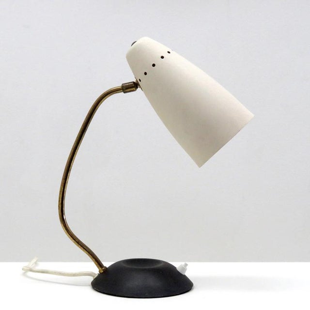 Elegant articulate table lamp, with matte black metal base, curved brass arm, orientable aluminium shade in textured...