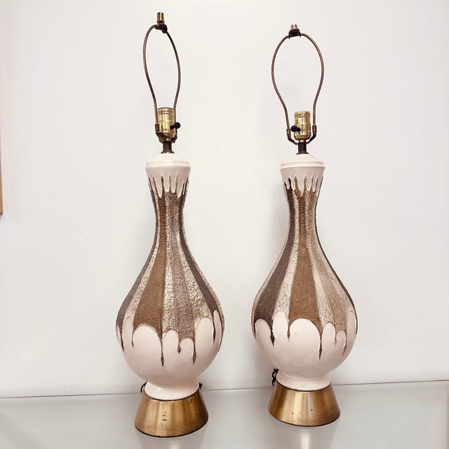 Pair of mid-century ceramic textured table lamps, off white with brass bases and earth tone details. Shades not included