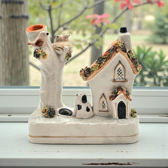 A charming Staffordshire style figural smoker modeled as a quaint cottage beside a hollow tree trunk, accented with...