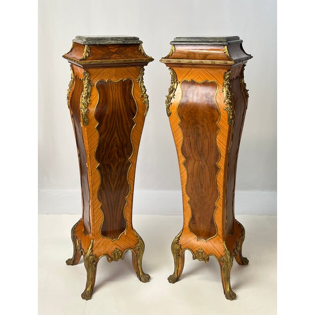A grand pair of mid-20th-century French Rococo Style pedestals, crafted with book-matched veneers and accented with...