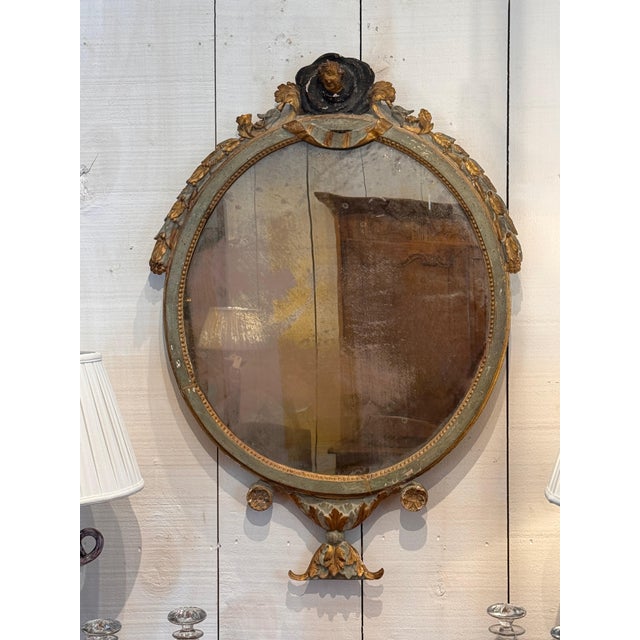 An oval mirror in an ornate gilt gesso frame in a period style, finished with green-painted ground and parcel-gilt...
